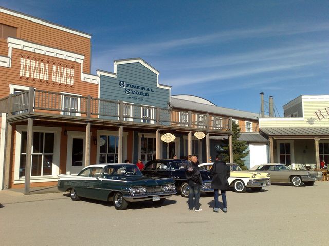 Green and white 1959 Oldsmobile Dynamic 88 parked next to other vintage cars in front of a General Store