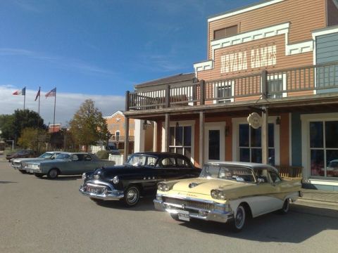 1991 Ford LTD Crown Victoria - A line of classic cars are parked on a street in front of buildings with a western architectural style.
