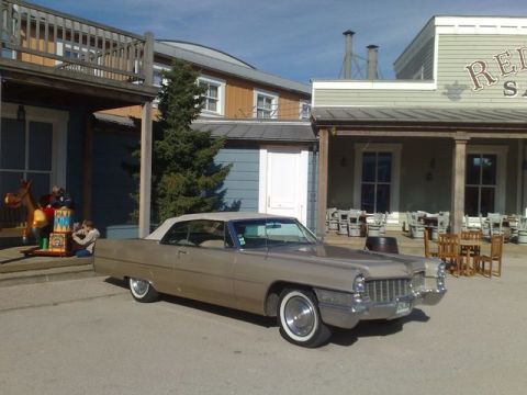 1991 Ford LTD Crown Victoria - A classic tan Cadillac convertible is parked in front of a western-themed building.