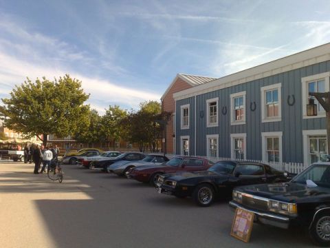 1991 Ford LTD Crown Victoria - A collection of vehicles are parked in front of a building with a western theme, under a partly cloudy sky.