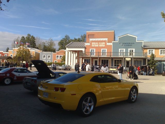 Yellow coupe parked in front of a western-themed building, with other cars visible