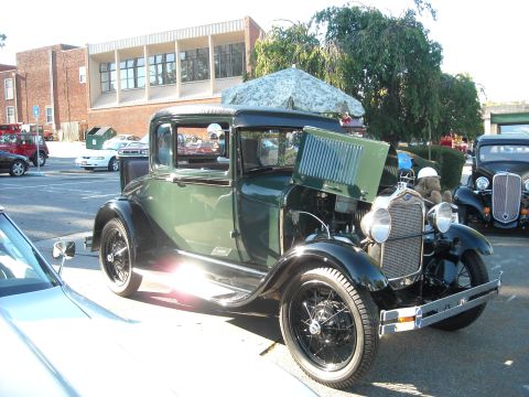 1979 Ford F-150 - A green 1928 Ford Model A coupe is displayed with its hood open at an outdoor car show.