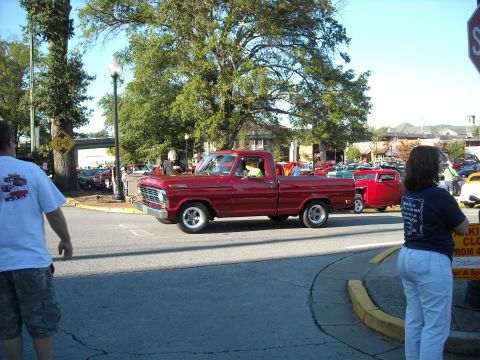 1979 Ford F-150 - A red pickup truck is seen driving down a street during a car show event.
