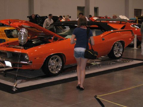 1968 Shelby GT500 - A woman walks past an orange convertible muscle car on display at an indoor event.