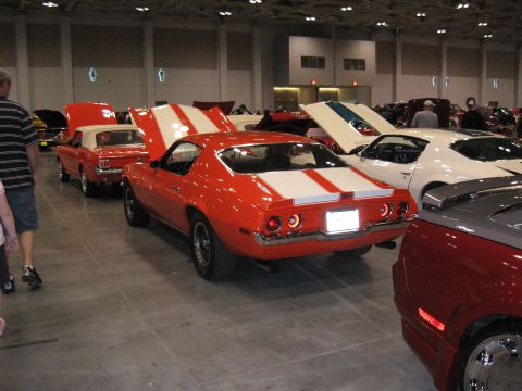 1968 Shelby GT500 - An orange muscle car with dual white racing stripes is parked at a car show.