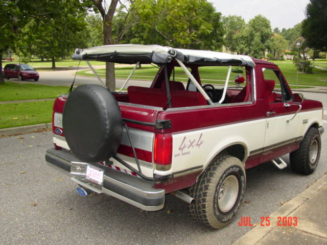Rear quarter of maroon and white Ford Bronco with soft top folded down and roll bar exposed