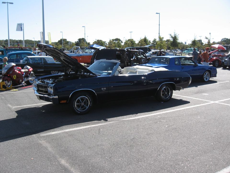 Dark blue convertible with hood open, parked in a lot with other cars and a motorcycle