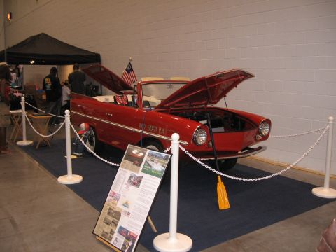 1968 Shelby GT500 - A red amphibious car is displayed indoors with its hoods open, showing a yellow paddle inside.