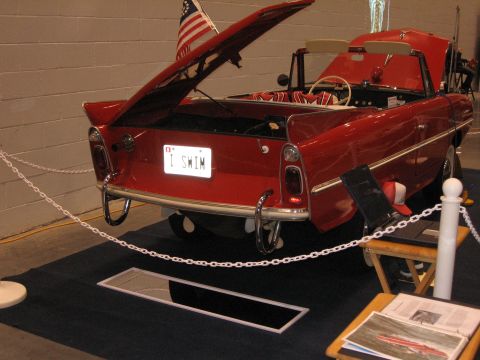 1968 Shelby GT500 - This red amphibious car, displayed at a car show, features an "I SWIM" license plate and its trunk is open.