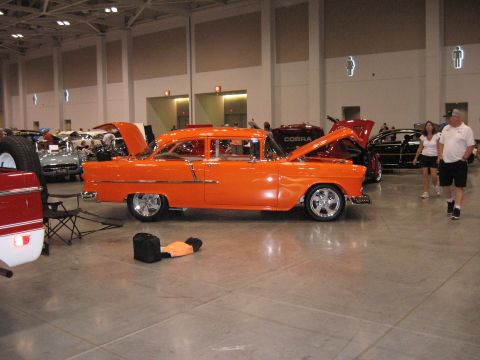 1968 Shelby GT500 - An orange 1955 Chevrolet Bel Air sedan is displayed indoors with its hood open, alongside other vehicles.