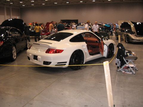 1968 Shelby GT500 - A white Porsche 911 is displayed indoors with its doors open, surrounded by other vehicles.