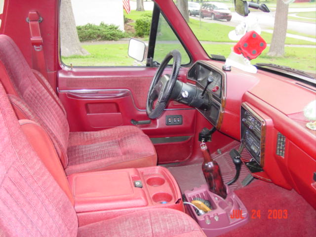 Red cloth interior of a truck with manual shifter, fuzzy dice on mirror, 2003 date stamp