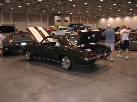 1968 Shelby GT500 - A dark brown 1969 Chevrolet Camaro is displayed with its hood and trunk open at an indoor car show.