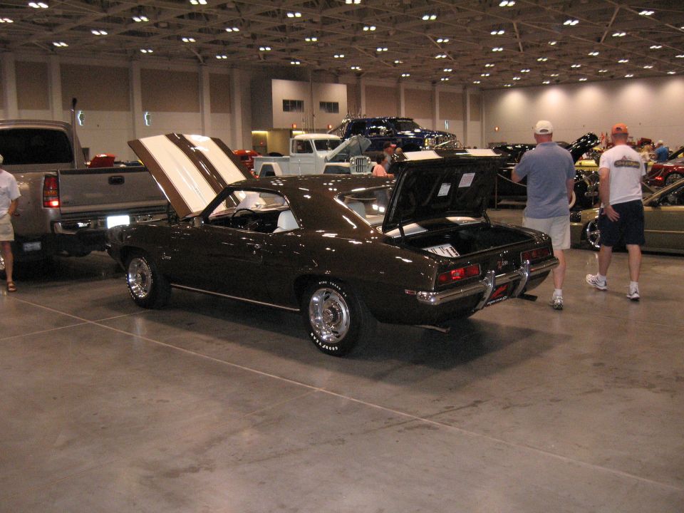 Dark brown 1969 Chevrolet Camaro with white racing stripes on the hood and trunk, viewed from the rear three-quarter angle