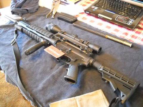 1996 Ford F-250 - AR-15 style rifle with scope and magazine laid out on a table with a laptop.