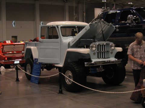 1968 Shelby GT500 - A light blue pickup truck with its hood open is displayed at a car show, with other vehicles visible in the background.