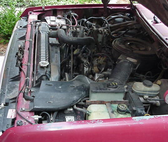 Engine bay of a maroon truck showing inline engine, radiator, hoses and brake master cylinder
