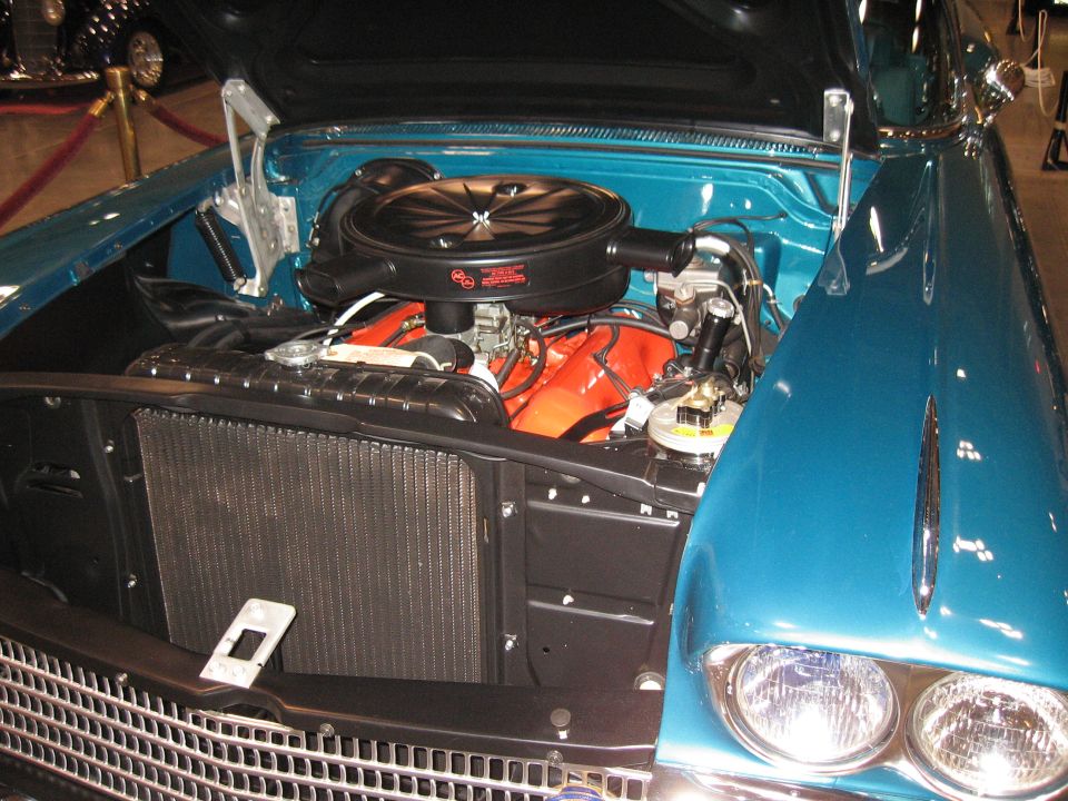 Teal car engine bay with orange V8 engine, black air cleaner, and chrome grille