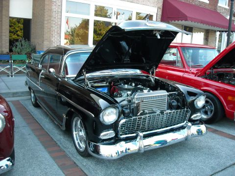 1979 Ford F-150 - A black 1955 Chevrolet Bel Air is displayed with its hood open, parked alongside a red vehicle at an outdoor event.