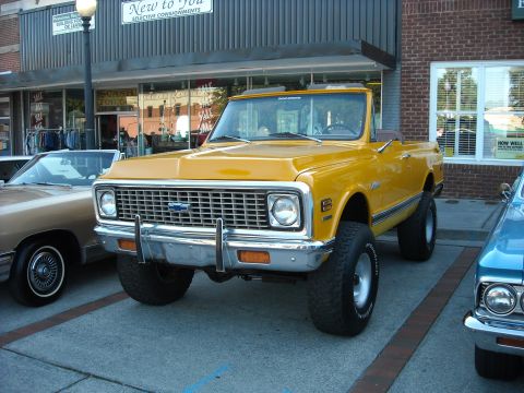 1979 Ford F-150 - A lifted yellow 1973 Chevrolet K5 Blazer is parked next to other vehicles in front of a store.
