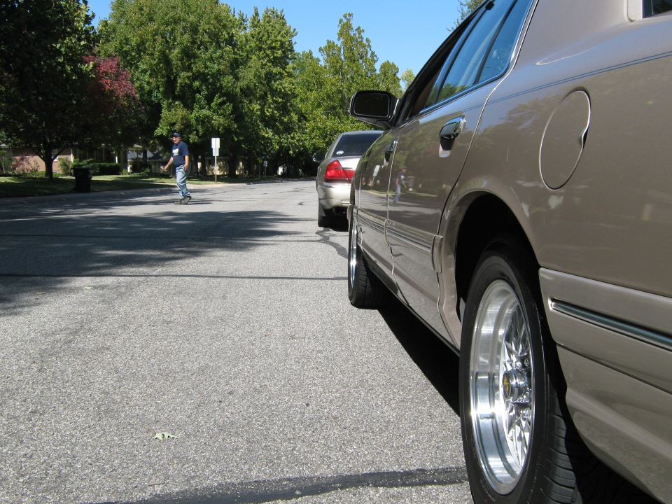 Tan 2000 Mercury Grand Marquis sedan, side view, chrome wheels, parked on asphalt street