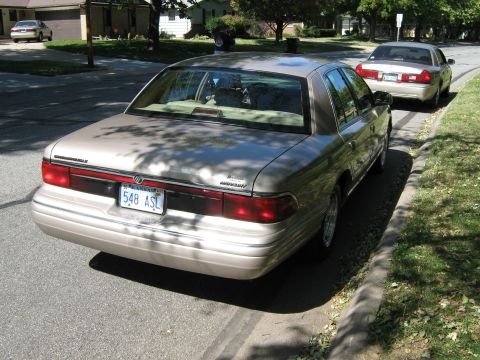 2000 Mercury Grand Marquis - Two Mercury Grand Marquis sedans are parked on a tree-lined street in a residential neighborhood.