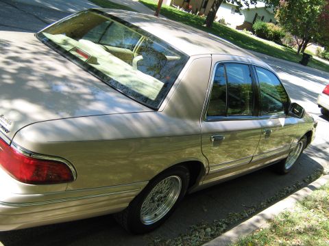 2000 Mercury Grand Marquis - A tan Mercury Grand Marquis is parked on the side of a street, with trees and houses in the background.