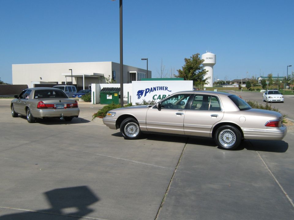 Two tan Mercury Grand Marquis sedans parked outside a building with a "PANTHER CAR" sign
