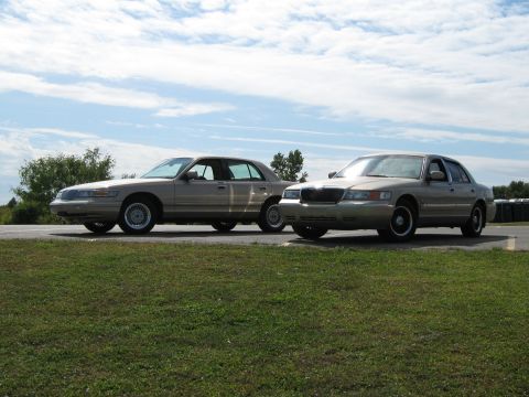 2000 Mercury Grand Marquis - Two tan 2000 Mercury Grand Marquis sedans are parked on asphalt under a cloudy sky.