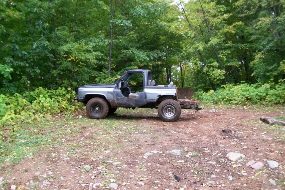 Off-road SUV with no doors parked in a wooded area. It has large tires and a trailer hitch