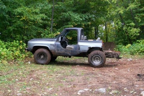 1988 Chevrolet Blazer - This modified SUV, likely from the 1980s, sits on a dirt path surrounded by trees.