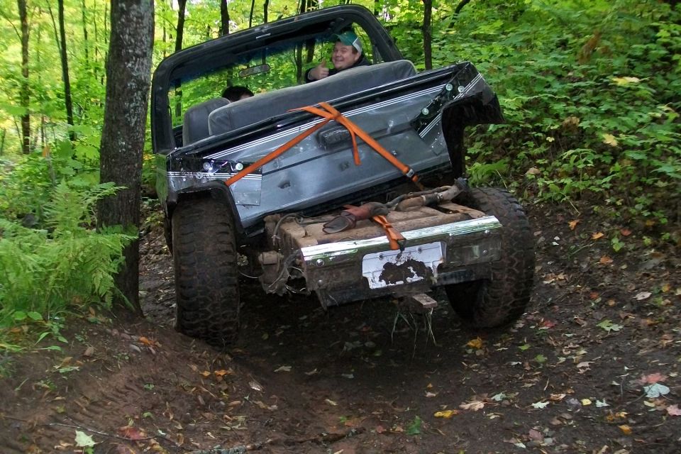 Jeep Wrangler with its rear end tilted up on a muddy trail, driver giving a thumbs up
