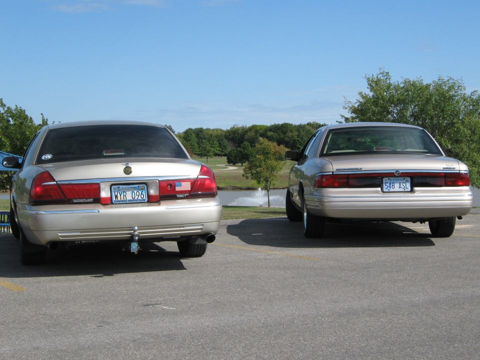 Two tan Mercury Grand Marquis sedans parked side-by-side, viewed from the rear. One has license plate WYR 096