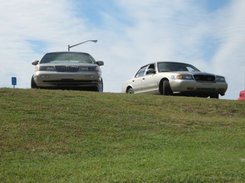 2000 Mercury Grand Marquis - Two 2000 Mercury Grand Marquis sedans are parked on a grassy incline under a cloudy sky.