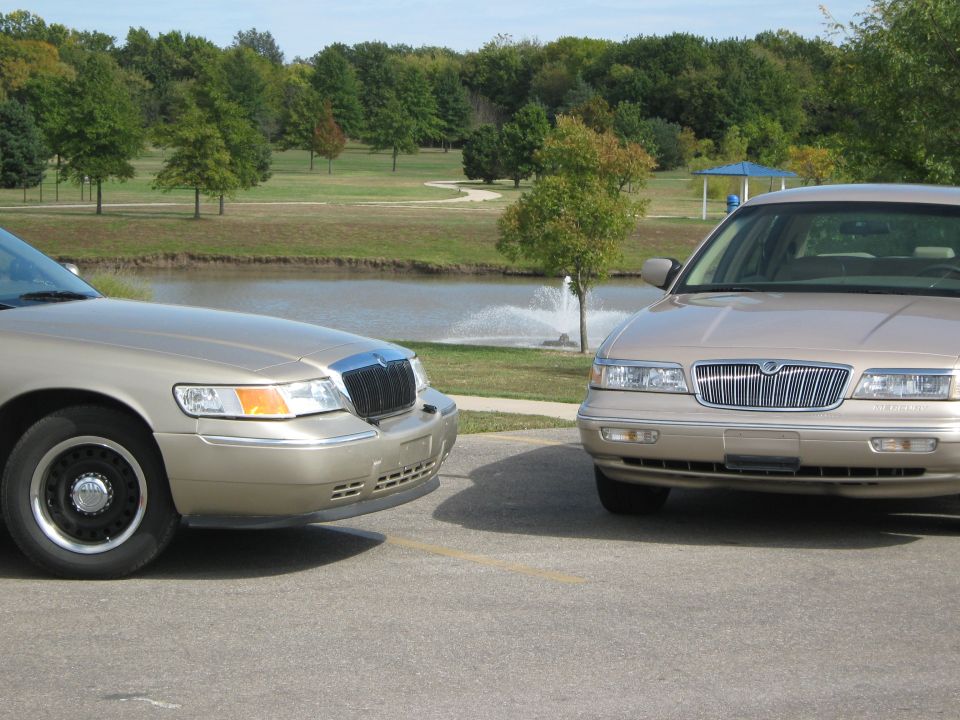 Two tan 2000 Mercury Grand Marquis sedans parked near a pond