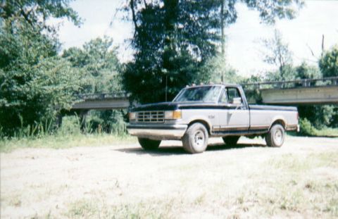 1987 Ford F-150 - This 1987 Ford F-150 pickup truck is parked outdoors near a bridge and trees.