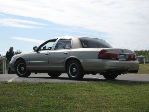 2000 Mercury Grand Marquis - A gold 2000 Mercury Grand Marquis is parked outdoors on a sunny day, viewed from the rear quarter angle.