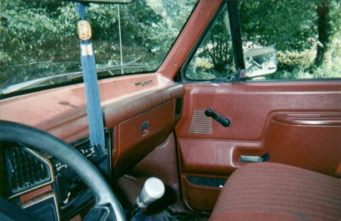 1987 Ford F-150 - The interior of a truck cab is shown, a red dashboard and door panels, with a gear shifter visible.