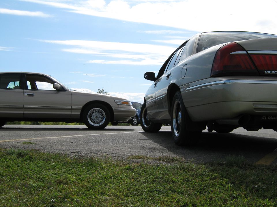 Two tan Mercury Grand Marquis sedans parked side-by-side on asphalt with grass in the foreground