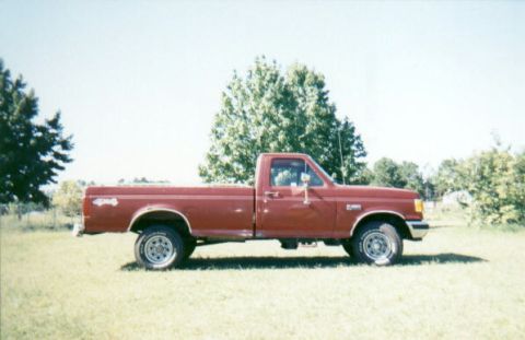 1987 Ford F-150 - This red 1987 Ford F-150 pickup truck is shown from the side, parked in a grassy field.