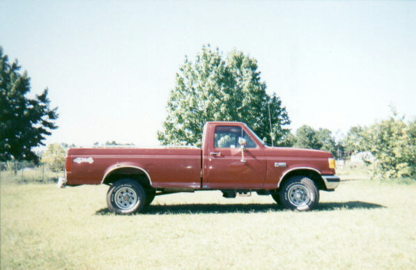 Dark red Ford F-Series regular cab long bed 4x4 pickup, passenger side view on grass