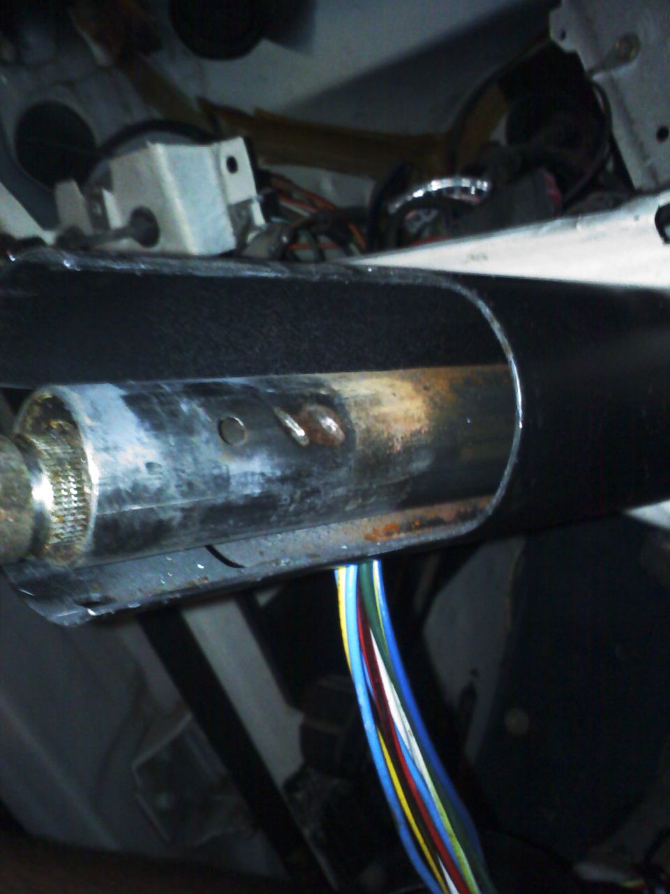 Close-up of steering column with exposed wiring harness. Shows metal and black plastic components