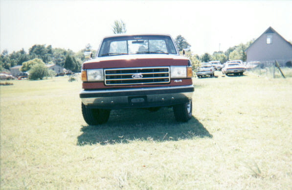 Front view of a red Ford F-Series pickup with bar grille and 4x4 badge parked on grass