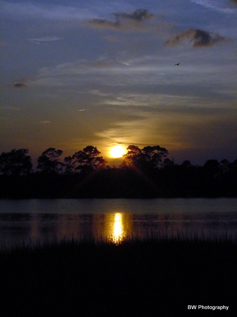 1996 Ford Bronco - The sun sets over the water, casting a reflection on the surface as clouds drift by.