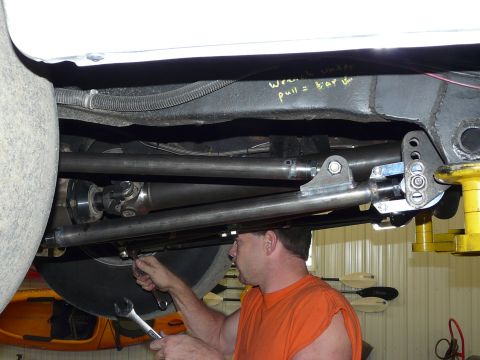 1994 Ford F-150 - A man in an orange sleeveless shirt works with a wrench under a raised white truck, adjusting a bare-steel four-link bar with adjustable ro…