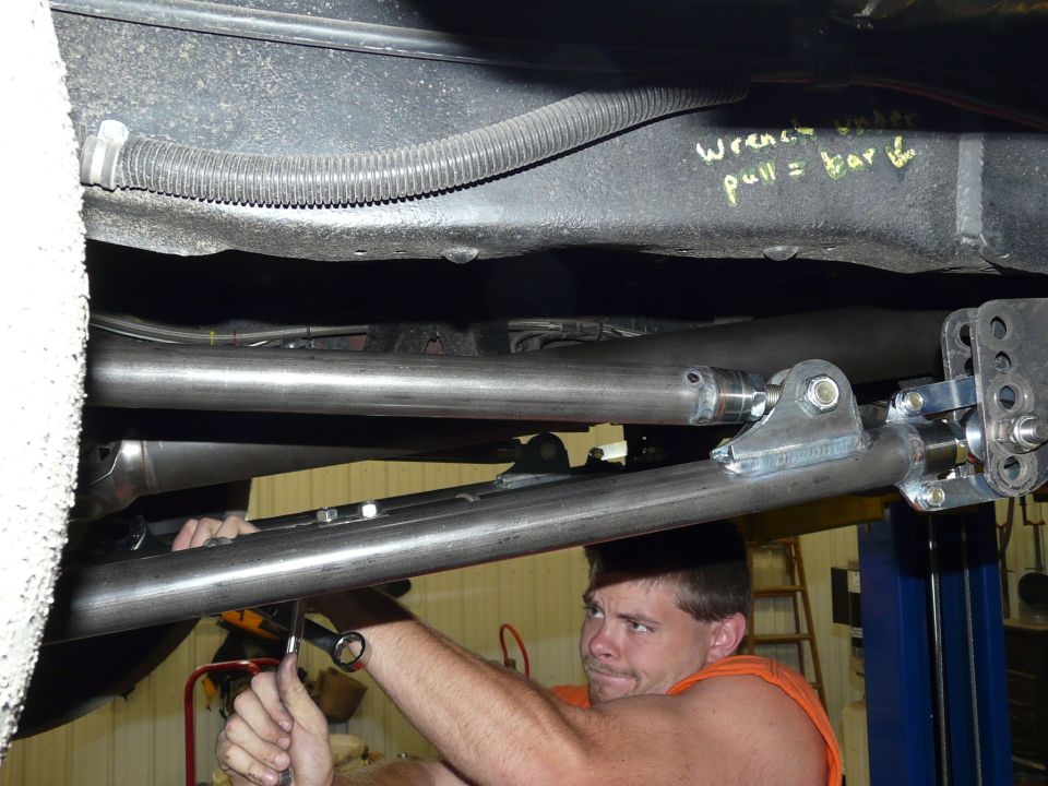 Underbody view of adjustable four-link bars and frame brackets with a man turning a wrench