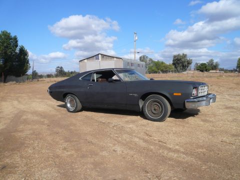 1975 Ford Ranchero - A matte black 1975 Ford Ranchero sits in a dry, dusty lot under a partly cloudy sky.