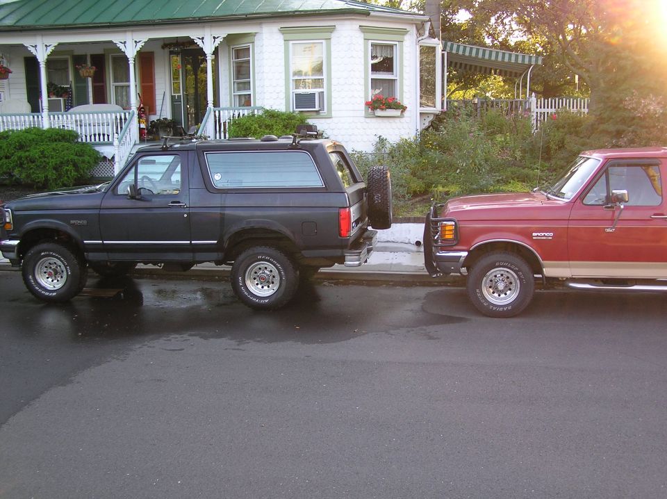 Dark gray Ford Bronco rear and red two-tone Ford Bronco front parked curbside