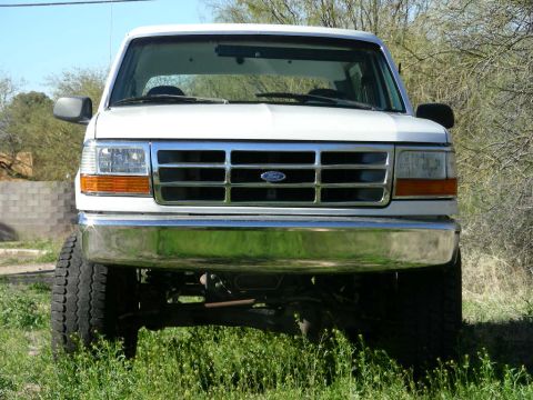 1996 Ford Bronco - Front view of a white Ford Bronco with a chrome bumper and grille, parked in grassy terrain.