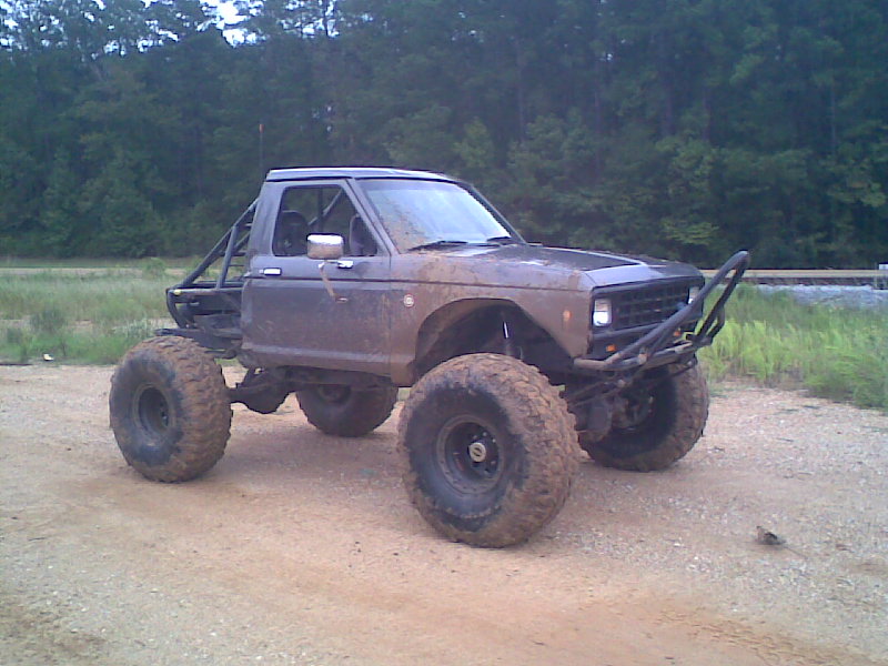 Lifted mud-covered Ford Bronco II on large off-road tires parked on gravel